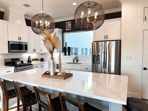 A modern kitchen with white cabinets, stainless steel appliances, and a large island with bar stools. - The Oasis Checkmate HTX Rooftop (Houston)