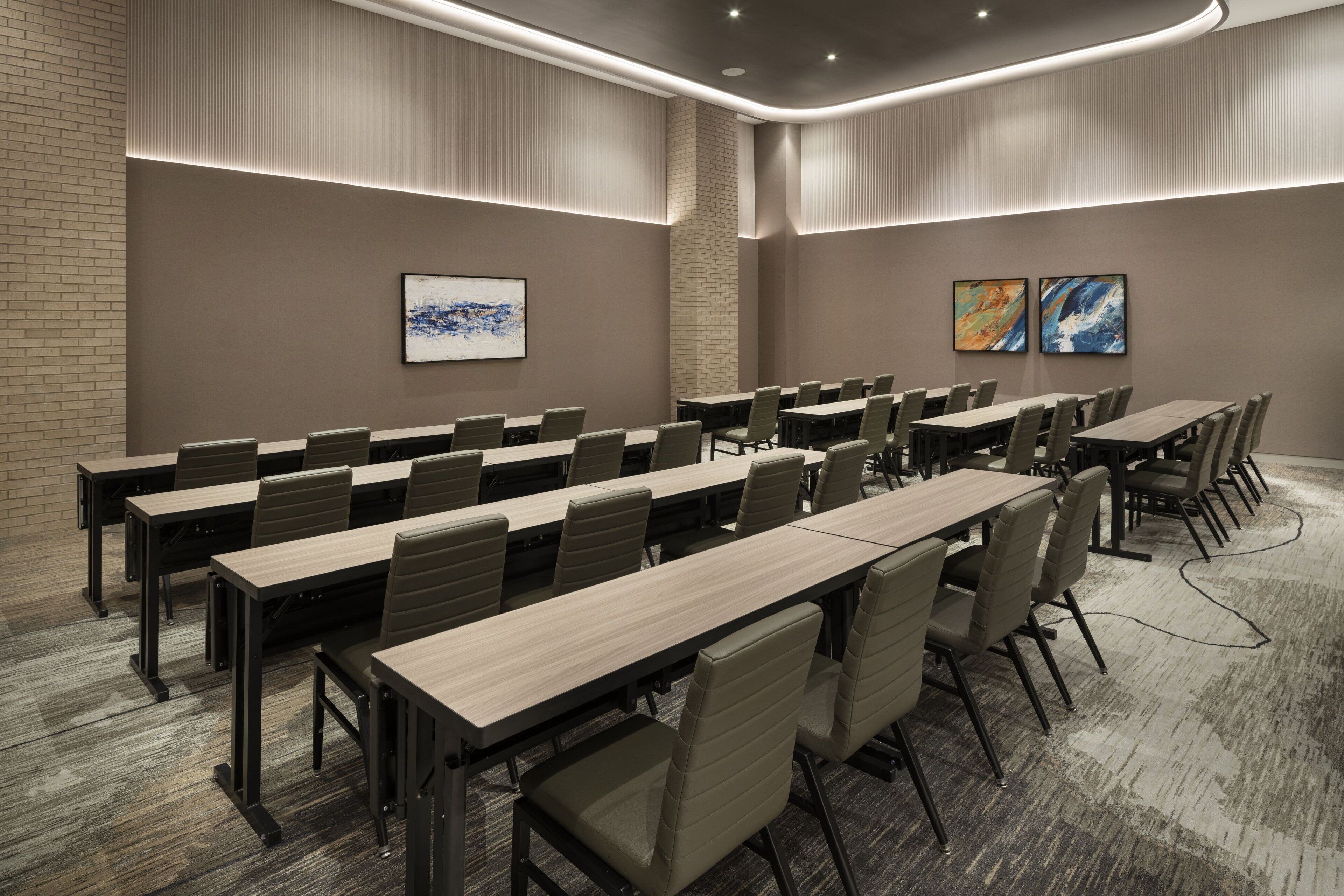 A conference room with long tables and chairs, a brick accent wall, and two abstract paintings.