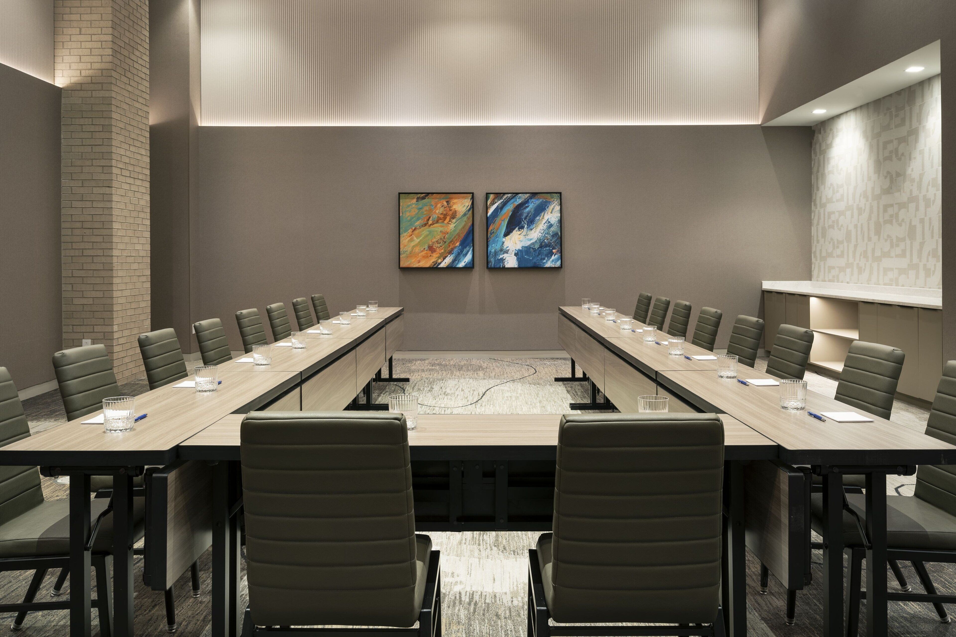 A conference room with a long table, multiple chairs, and two abstract paintings on the wall.