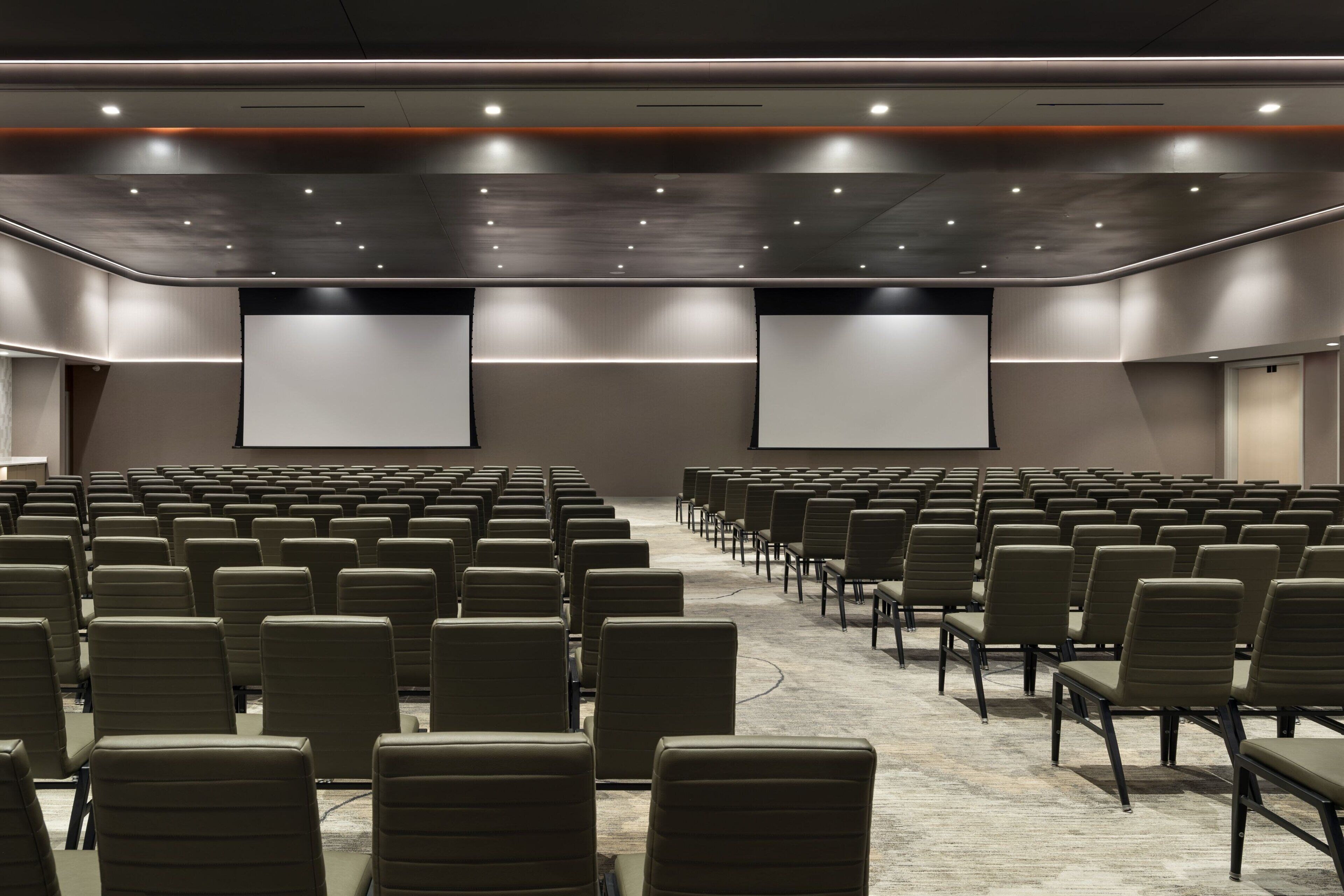 A conference room with rows of chairs, a carpeted floor, and a large screen at the front.