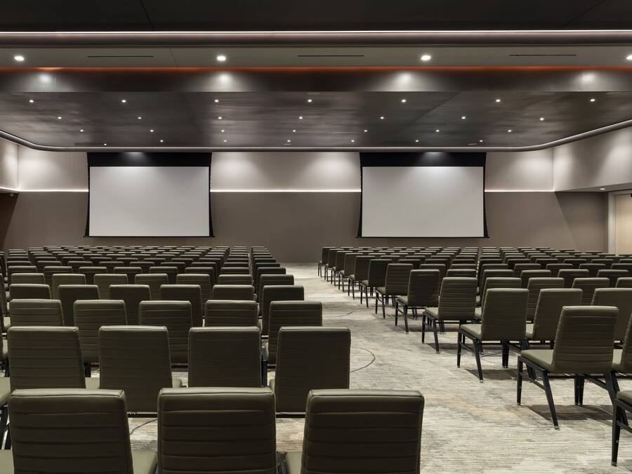 A conference room with rows of chairs, a carpeted floor, and a large screen at the front.