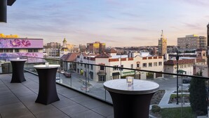 A balcony with tables and chairs overlooking a cityscape with buildings and a tower. - Cascade Hotel, Kansas City, a Tribute Portfolio Hotel (Kansas City)