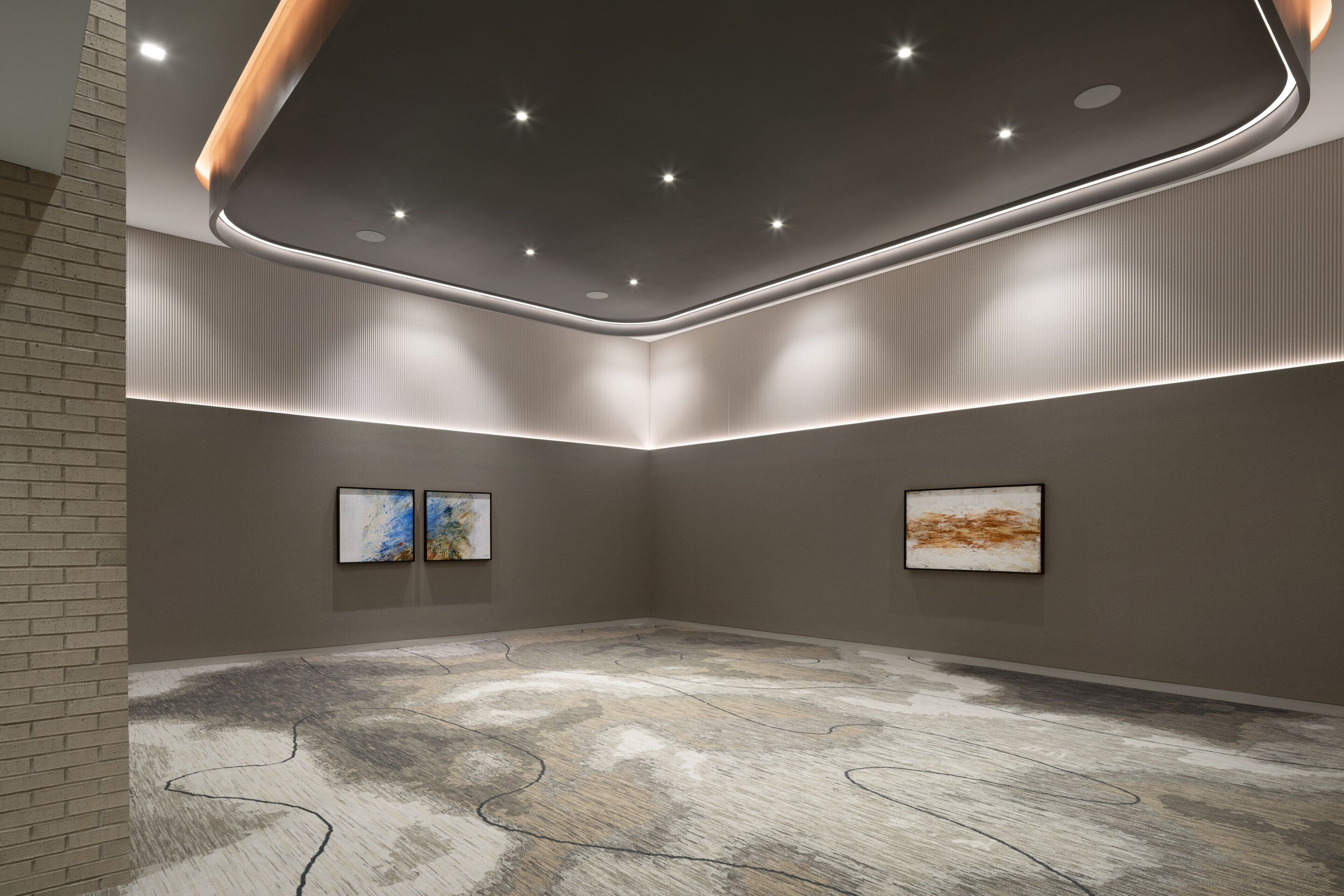 A modern art gallery with a minimalist design, featuring a textured floor, recessed lighting, and two framed artworks on the walls.
