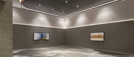 A modern art gallery with a minimalist design, featuring a textured floor, recessed lighting, and two framed artworks on the walls.