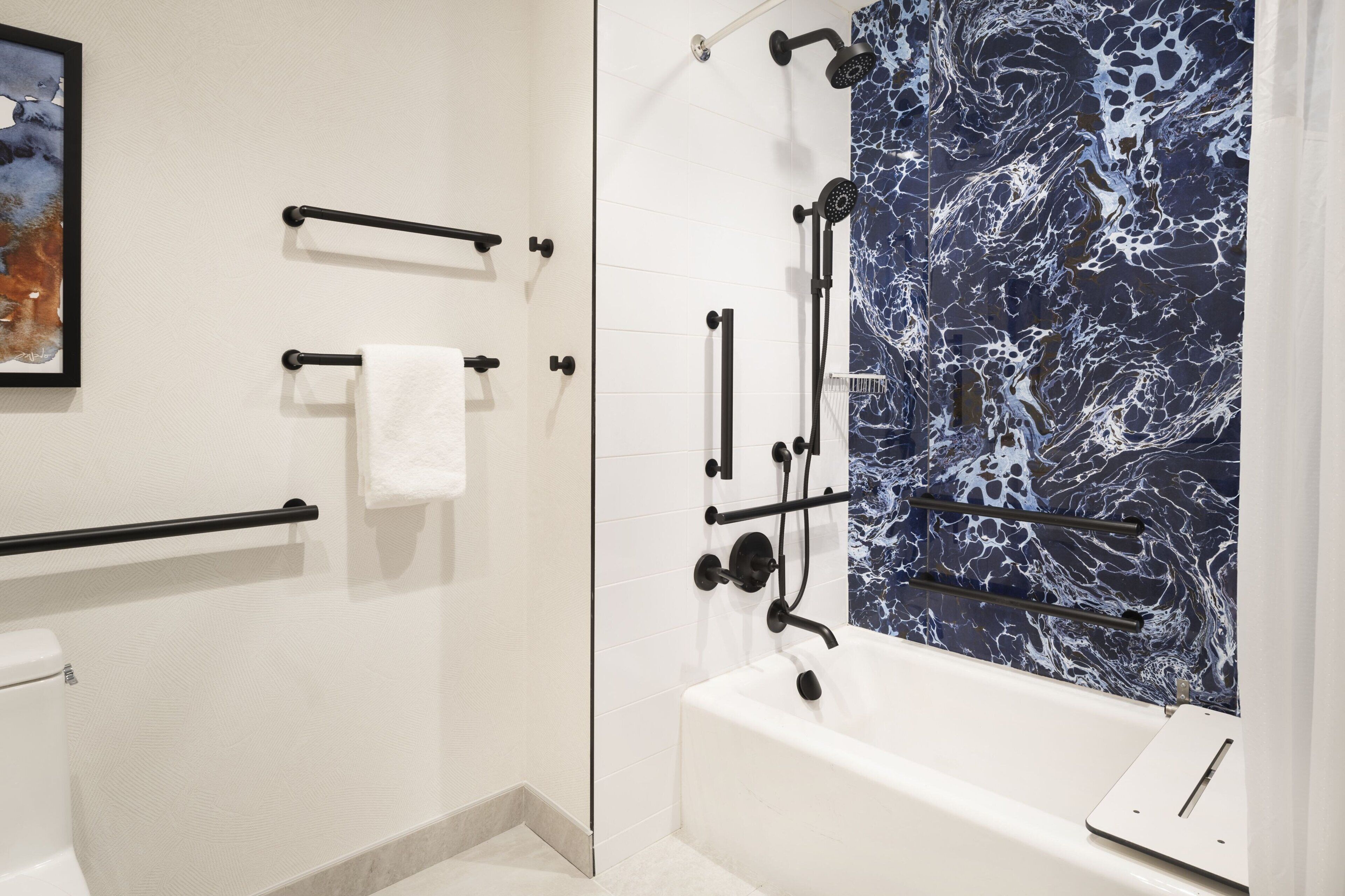 Une salle de bain moderne avec une baignoire blanche, des accessoires noirs et un mur de douche à motifs de marbre.
