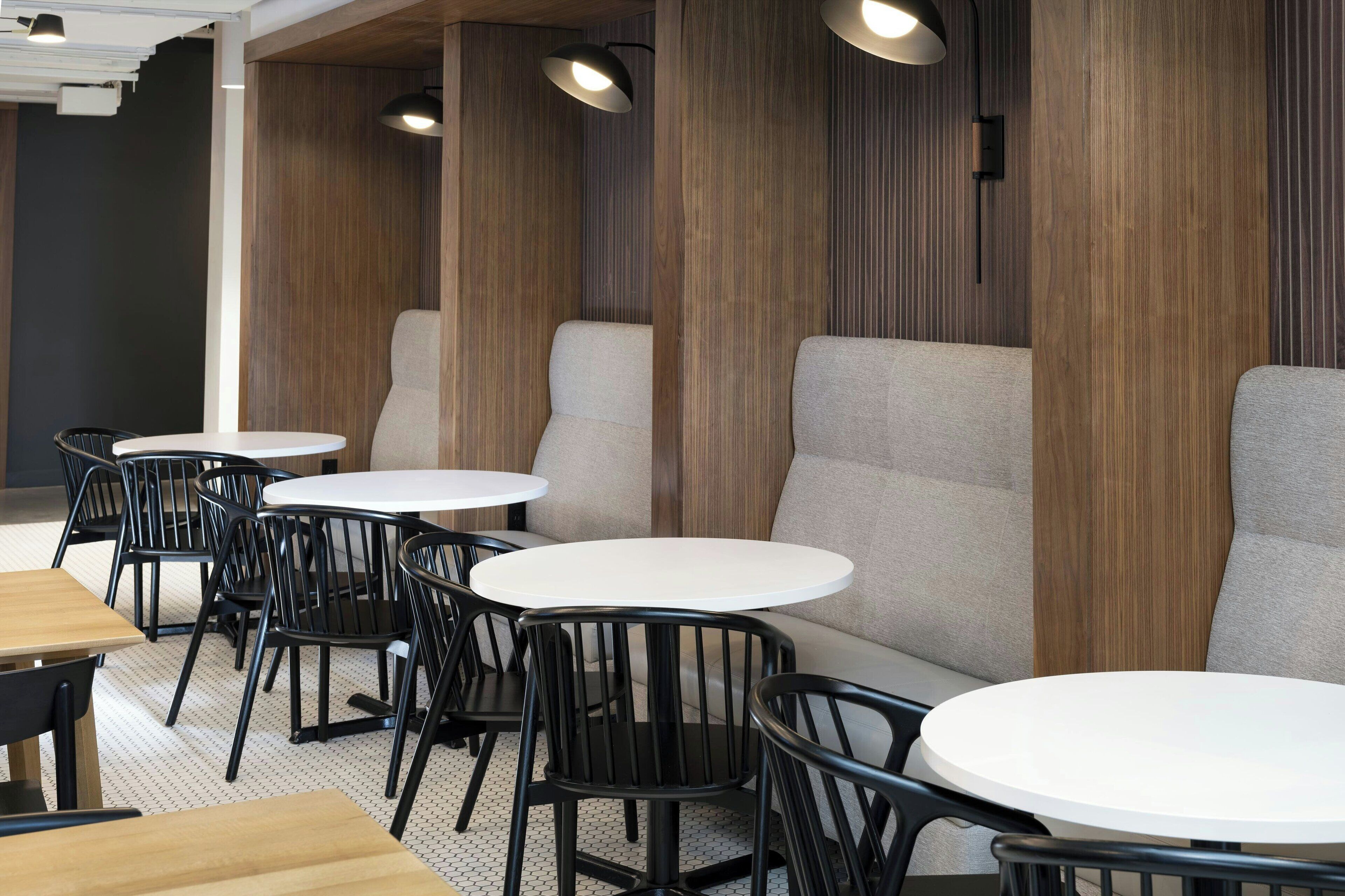 Un intérieur de restaurant moderne avec des tables rondes, des chaises noires et des murs recouverts de panneaux en bois.
