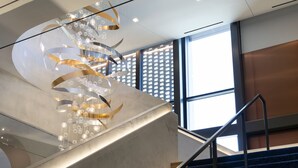 A modern staircase with a unique spiral light fixture and a view of the outside through large windows. - Cascade Hotel, Kansas City, a Tribute Portfolio Hotel (Kansas City)