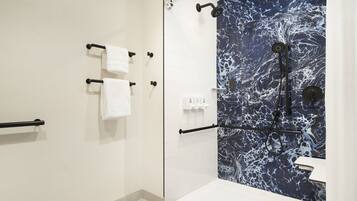 A modern bathroom with a glass shower enclosure, white tiled walls, and a marble backsplash.