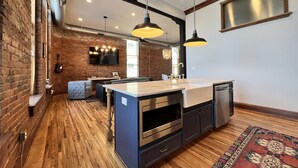 Una cocina moderna con una isla central, suelo de madera y pared de ladrillo rústico.