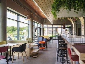 Ein modernes Restaurant mit Barbereich, großen Fenstern und Zimmerpflanzen.