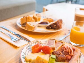 A breakfast setting with a plate of assorted foods, a glass of orange juice, and cutlery on a wooden table. - Greet Hotel Cernay Mulhouse (Cernay)