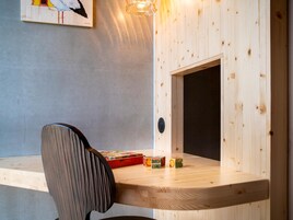 Un escritorio de madera con una silla, un ventanal pequeño y una lámpara de pared.