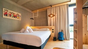 Un lit en bois avec une literie blanche, un luminaire suspendu, un sac à dos bleu et un tableau accroché au mur.