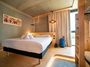 A wooden bed with white bedding, a hanging light fixture, a blue backpack, and a painting on the wall. - Greet Hotel Cernay Mulhouse (Cernay)