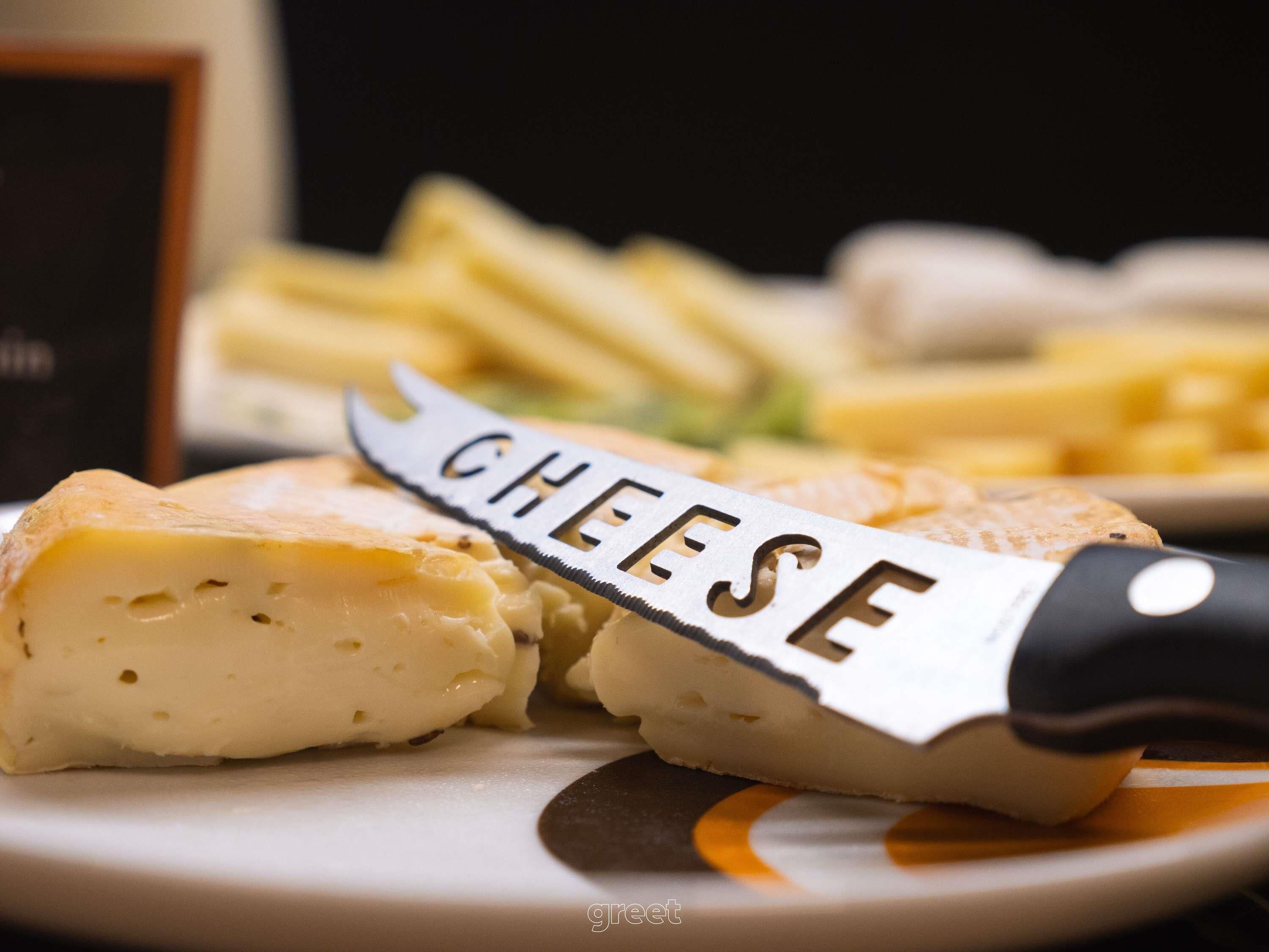 A close-up of a cheese wheel with a knife labeled "CHEESE" on a plate, accompanied by some cheese slices and a dish of fries.