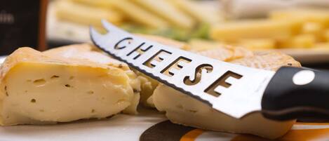 A close-up of a cheese wheel with a knife labeled "CHEESE" on a plate, accompanied by some cheese slices and a dish of fries.