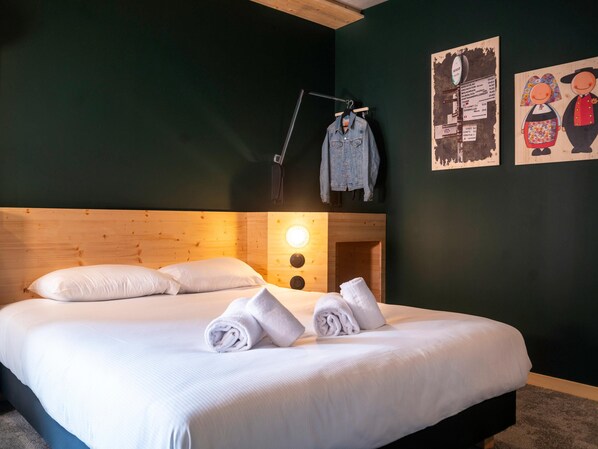 A neatly made bed with white linens and rolled towels, a wooden headboard, a wall clock, and a poster of cartoon characters. - Greet Hotel Cernay Mulhouse (Cernay)