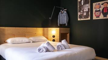 Ein ordentlich bezogenes Bett mit weißen Leinen und aufgerollten Handtüchern, ein Holz-Kopfteil und eine Wanduhr.