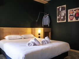 Una cama bien hecha con sábanas blancas y toallas enrolladas, un cabecero de madera y un reloj de pared.