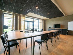 Una sala conferenze con un lungo tavolo, sedie, una lavagna e un televisore.
