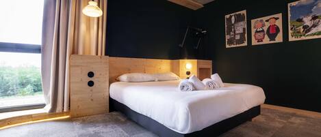 A modern hotel room with a large bed, wooden headboard, and a view of the outdoors.