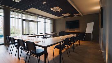 A conference room with a long table, chairs, a whiteboard, and a TV on the wall.