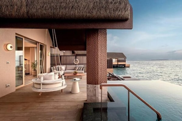 A luxurious outdoor lounge area with a pool, seating, and a view of the sea.