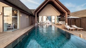 Una piscina con sillas de descanso, un espacio de estar techado y un edificio con amplias ventanas.