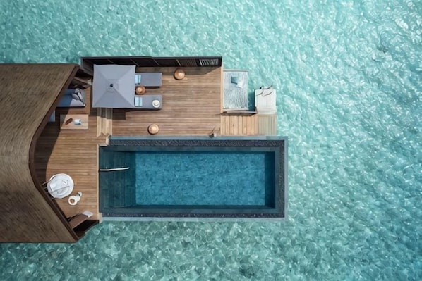 An aerial view of a resort with a swimming pool, wooden deck, and lounge area.