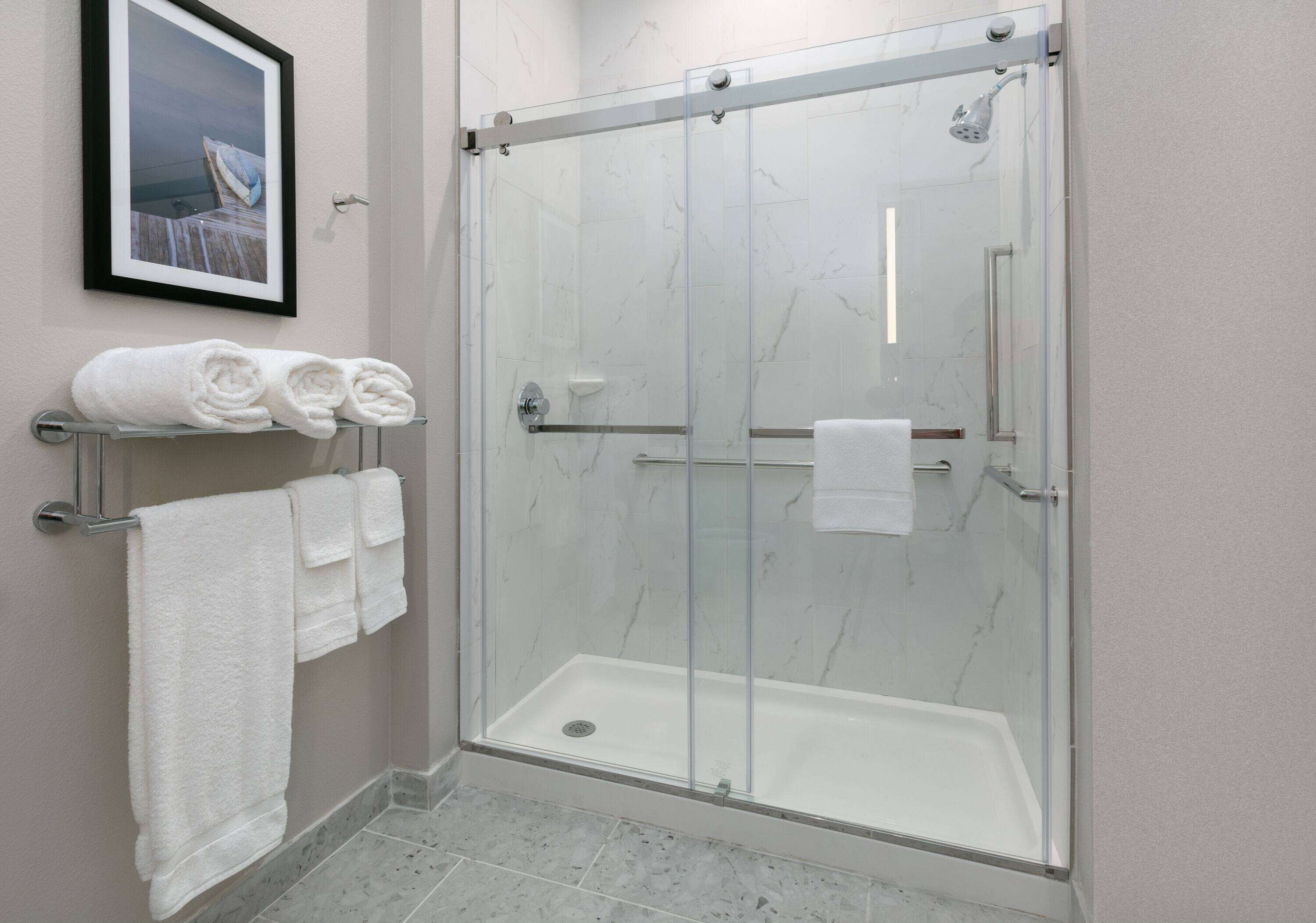 A glass-enclosed shower with a white marble floor and a framed picture on the wall.