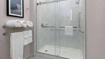 A glass-enclosed shower with a white marble floor and a framed picture on the wall.
