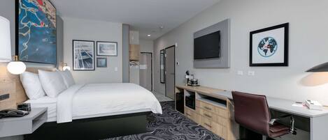 A modern hotel room with a bed, desk, chair, and artwork on the walls.