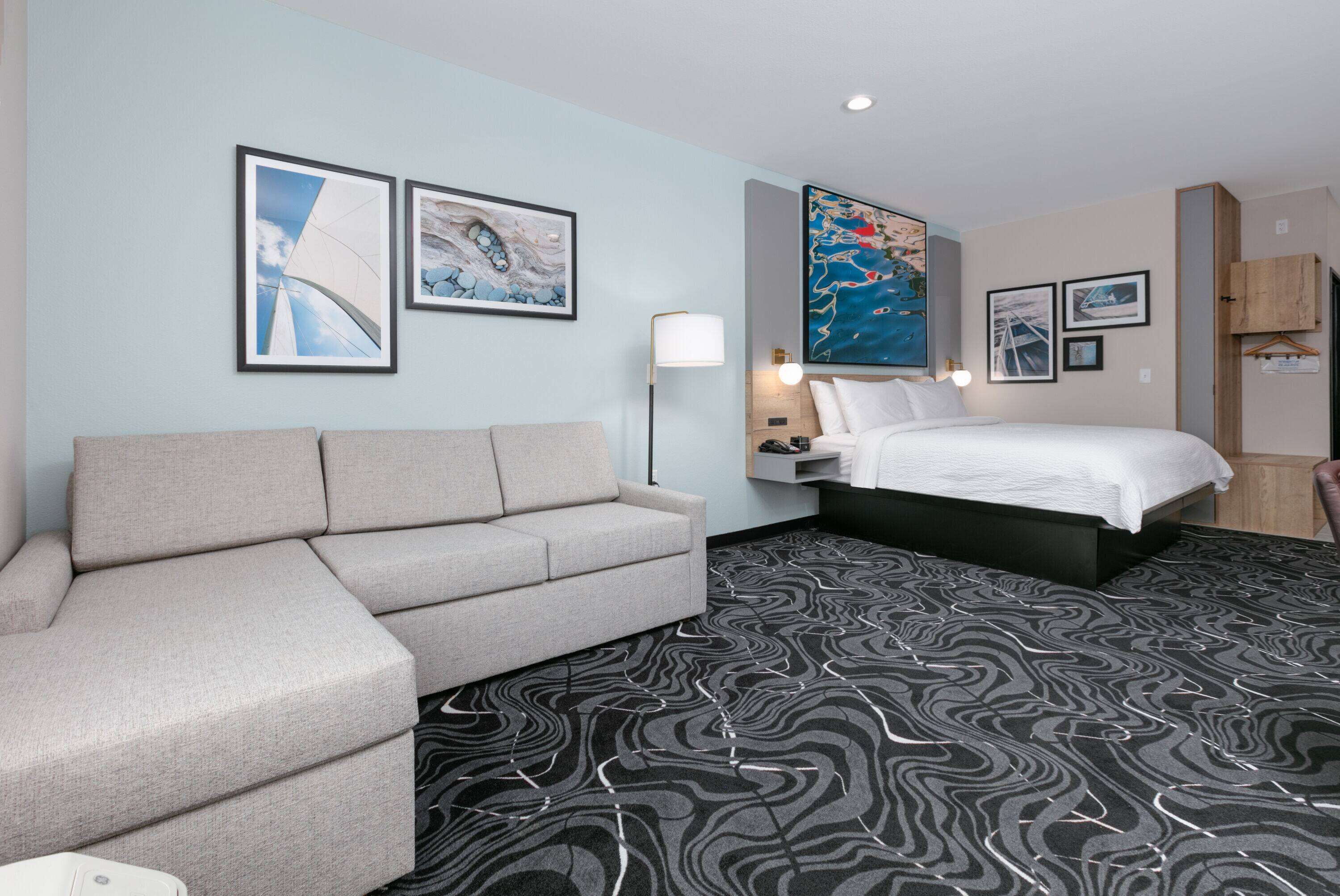 Een hotelkamer met een bank, een bed, een kamerbreed tapijt met dessin en kunstwerken aan de wanden.