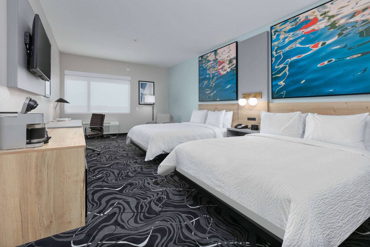 A hotel room with two beds, a desk, a TV, and artwork on the walls.