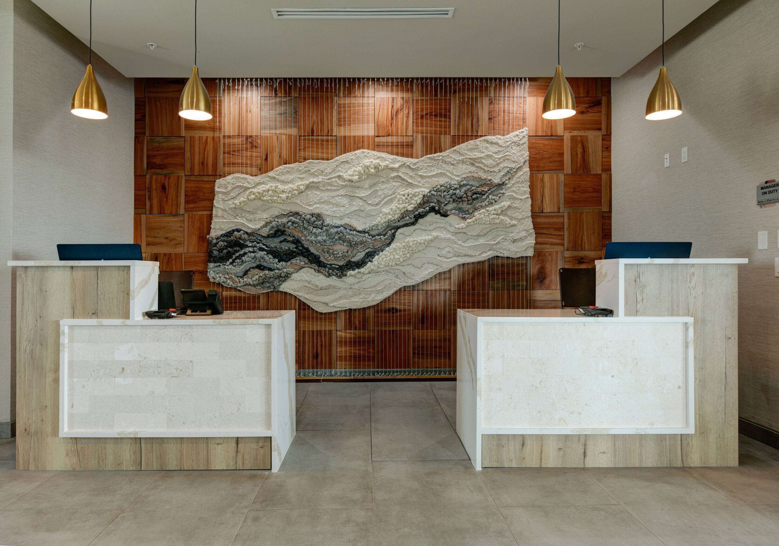 A reception area with a large textured wall art, two reception desks, and pendant lighting.