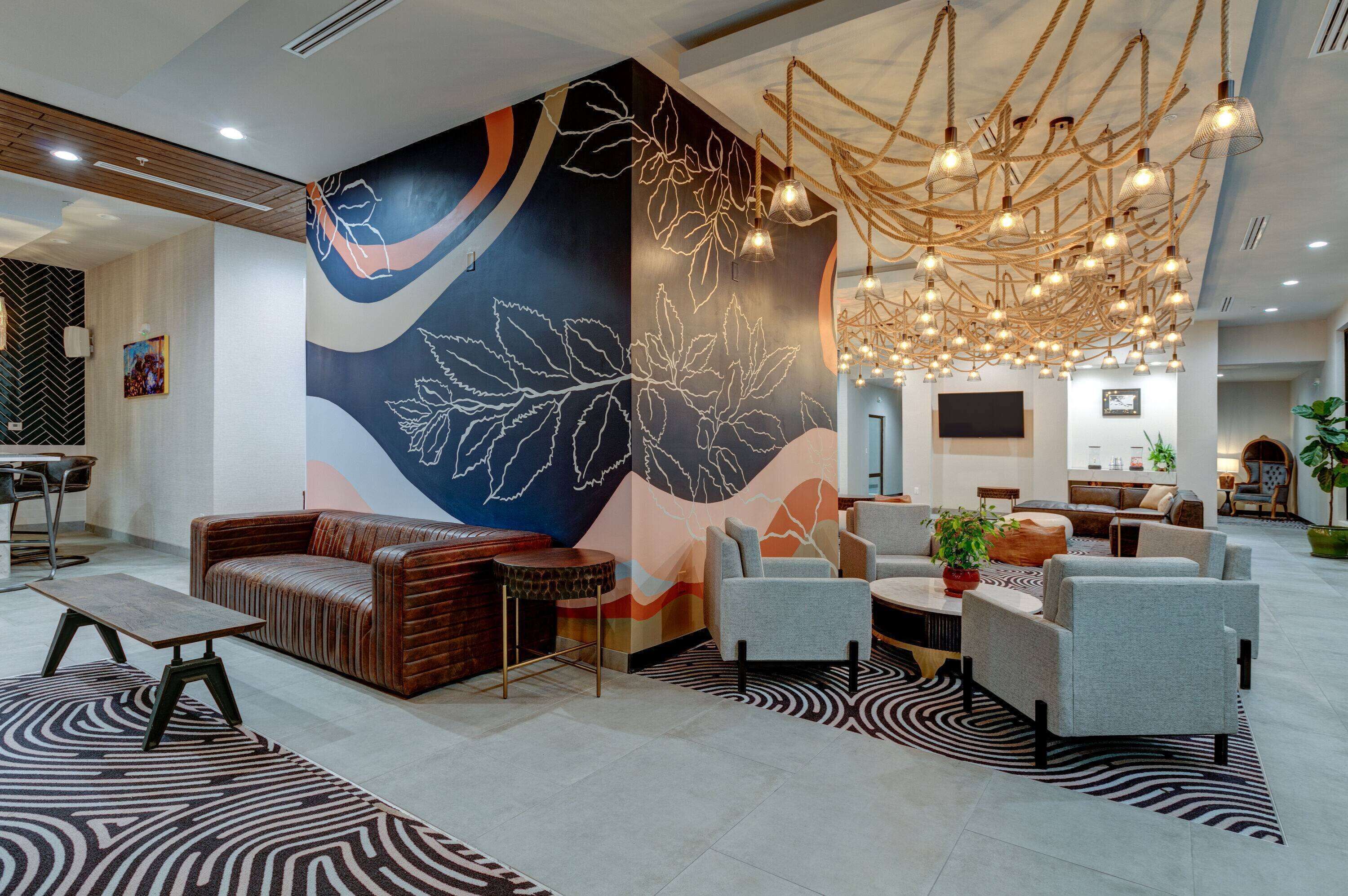 Eine moderne Lobby mit einer großen Wandmalerei, einer Sitzecke und einem außergewöhnlichen Kronleuchter.