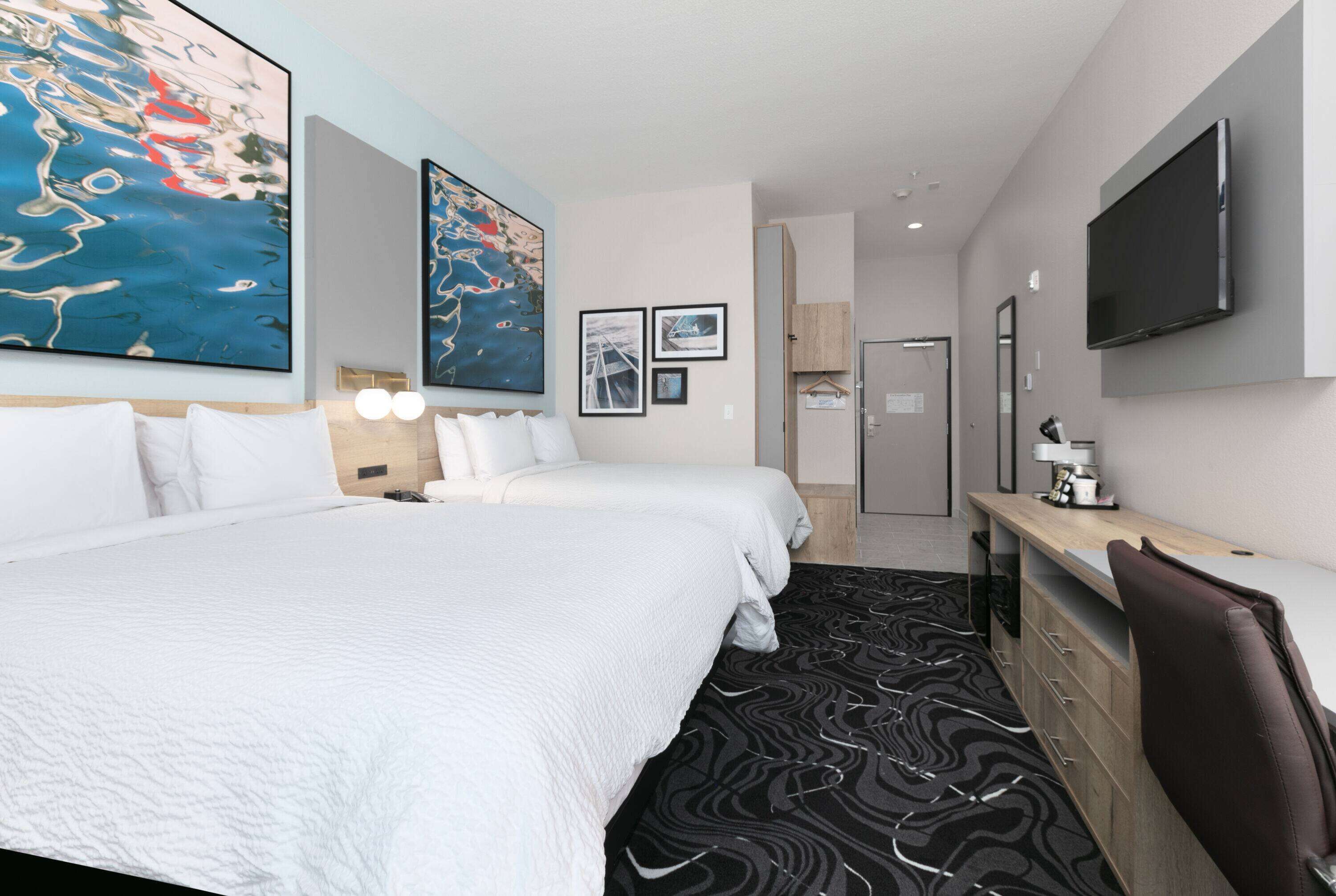 A hotel room with a large bed, a desk, a TV, and artwork on the walls.