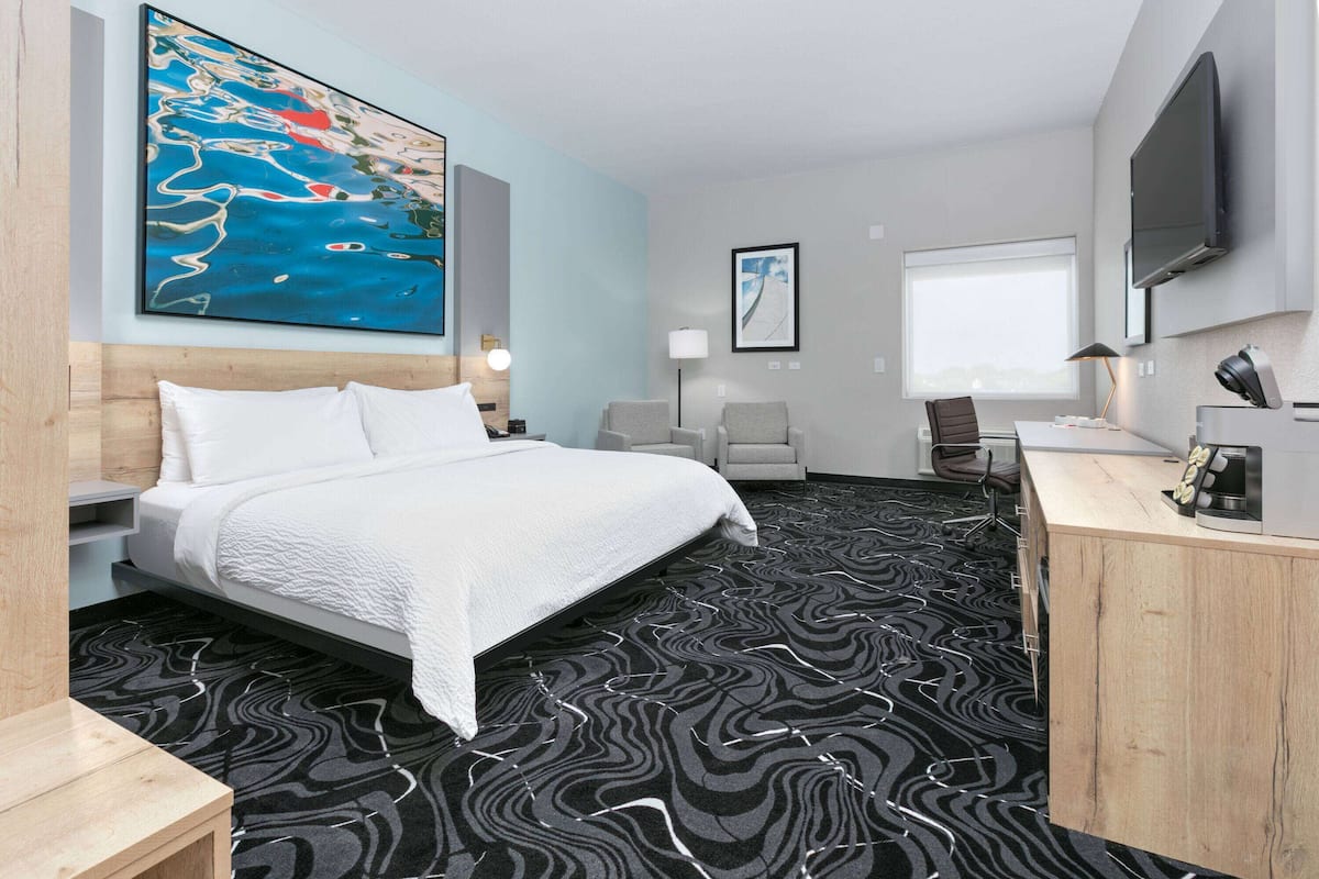 A hotel room with a large bed, a desk, a chair, a TV, and artwork on the walls.
