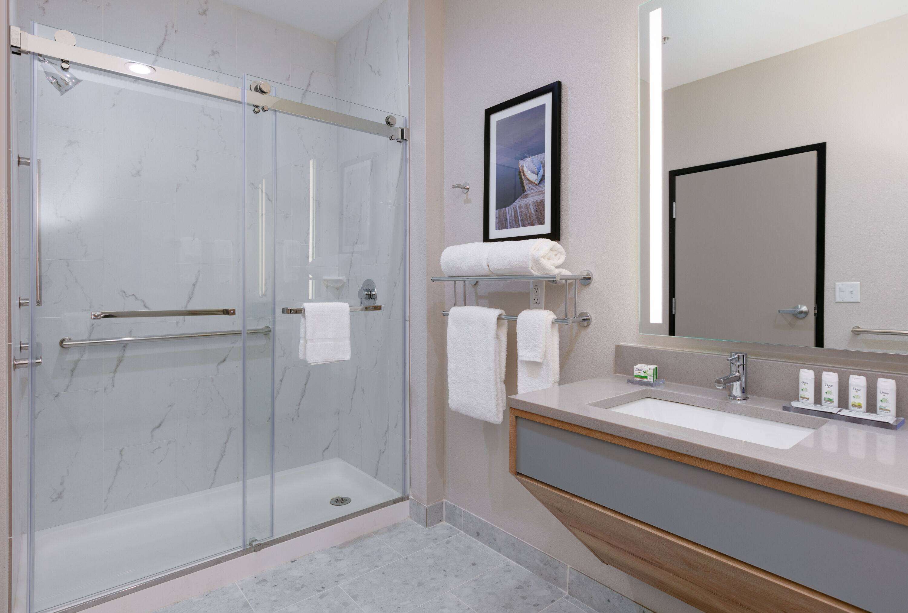 Une salle de bain moderne avec une douche à parois de verre, un meuble-lavabo avec un évier et un miroir, et un tableau encadré au mur.