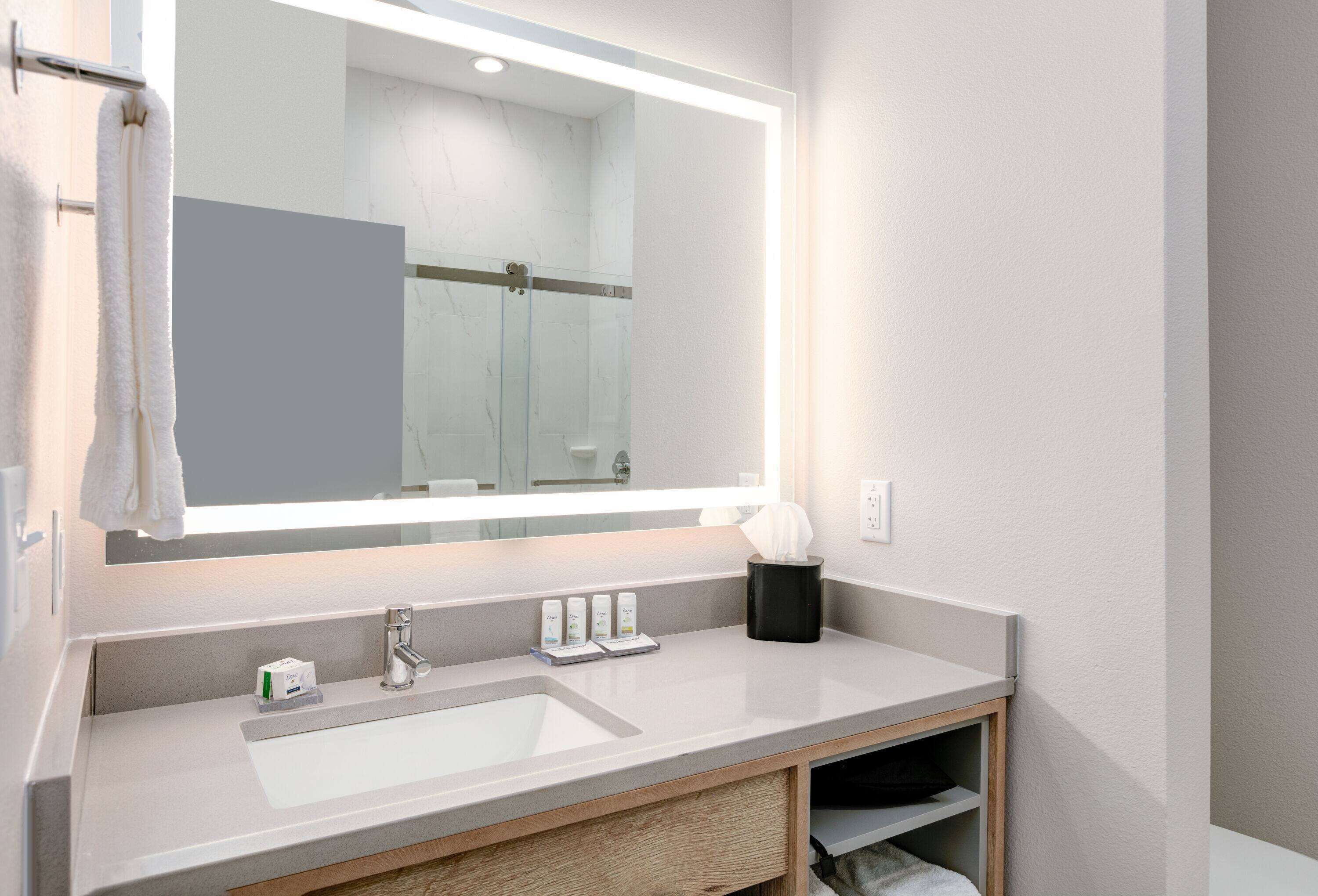 A modern bathroom with a large mirror, a white sink, and a towel rack.