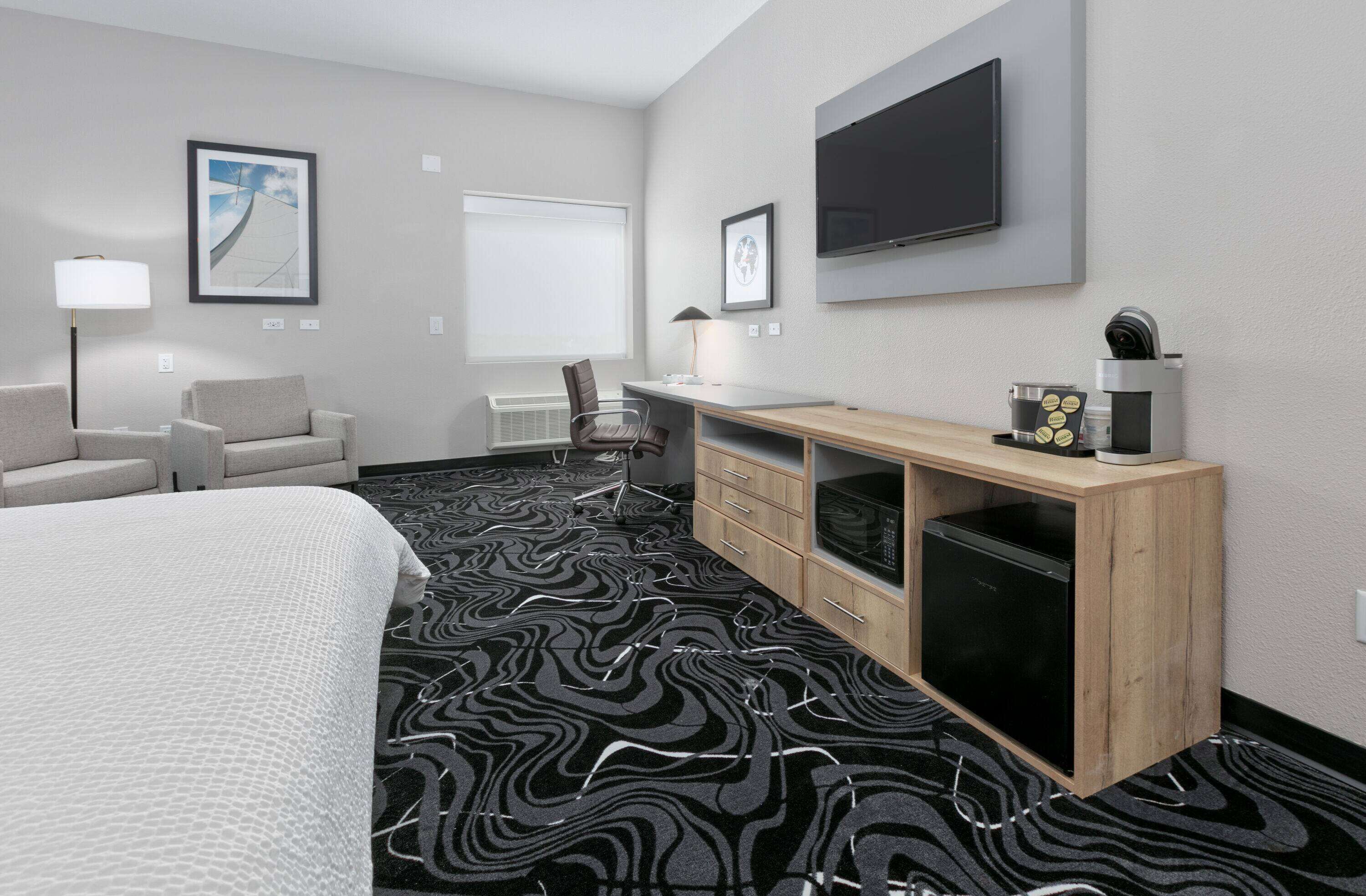 A hotel room with a bed, a desk, a chair, a TV, and a microwave.