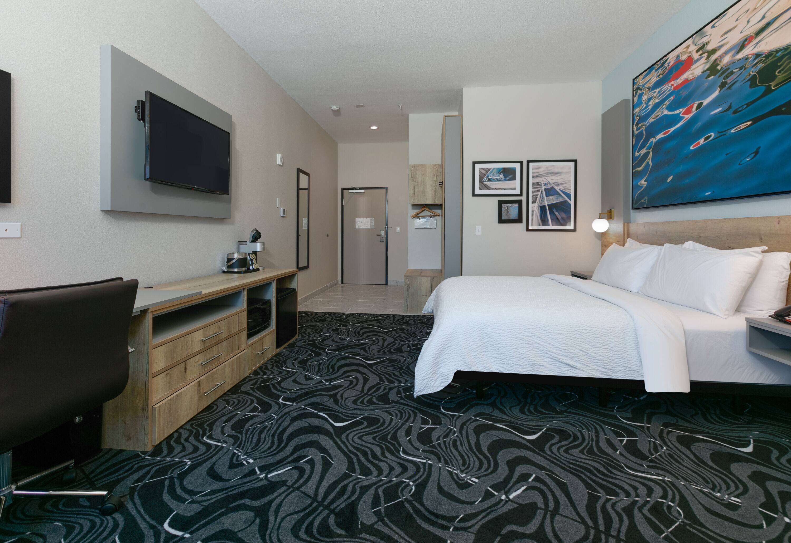 A hotel room with a bed, a desk, a TV, and a painting on the wall.