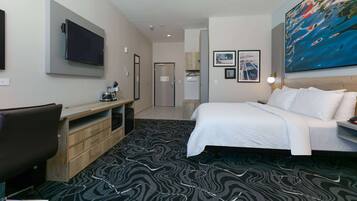 A hotel room with a bed, a desk, a TV, and a painting on the wall.
