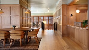 Amplia zona de recepción con un mostrador de madera, un área de asientos con sillas de mimbre y vistas del interior a través de una puerta de cristal.