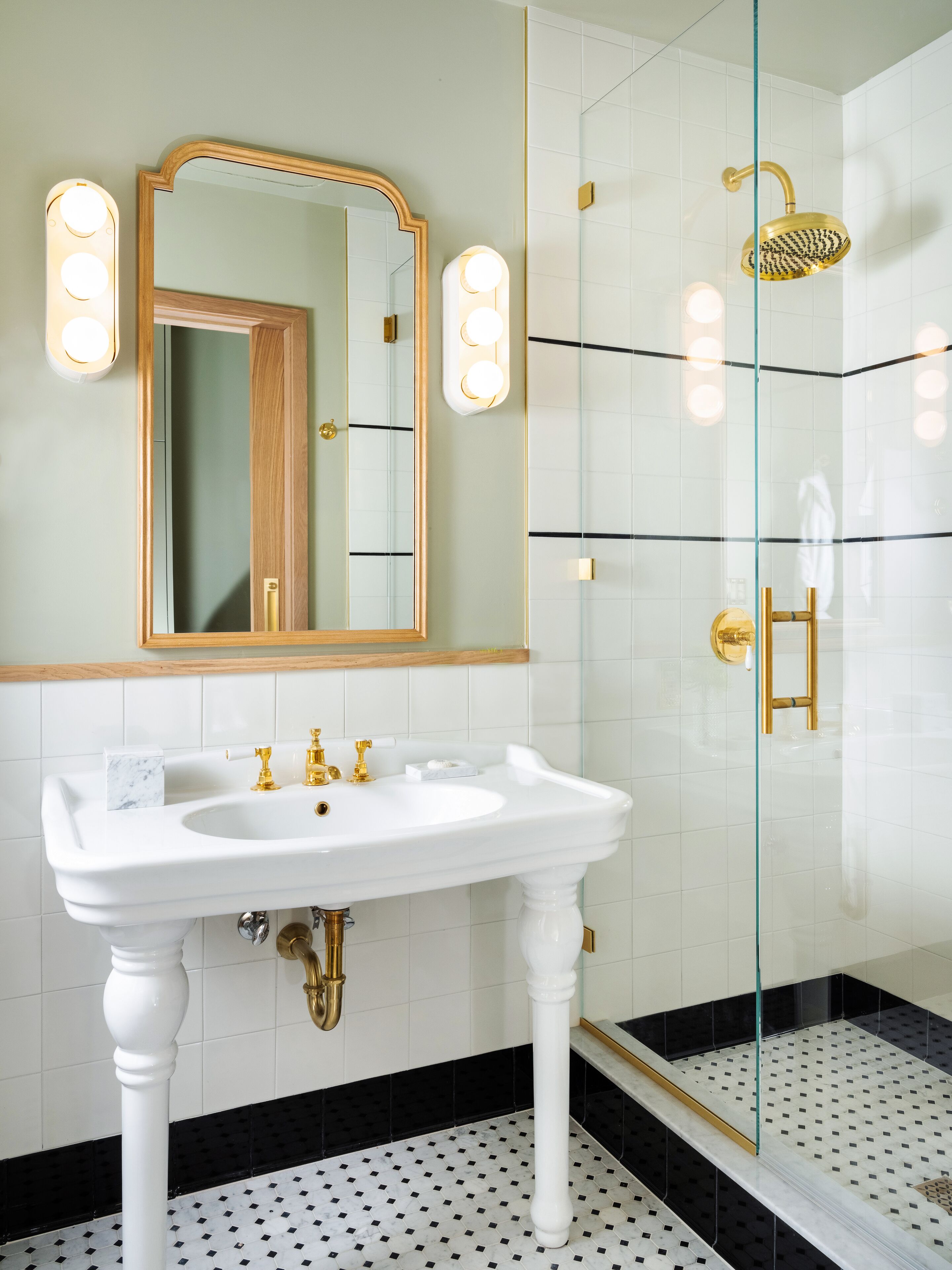 A bathroom with a white sink, gold fixtures, a large mirror, and a glass-enclosed shower.