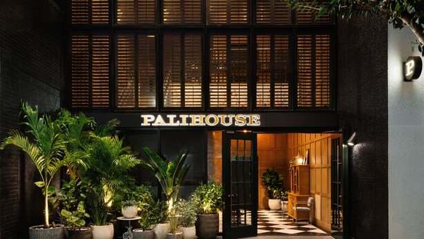 Un edificio con el letrero "PALIHOUSE" en la entrada, que tiene un suelo de cuadros y plantas en macetas.
