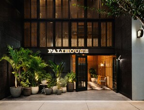 Een gebouw met het bord "PALIHOUSE" bij de ingang, met een zwart-wit geruite vloer en potplanten.