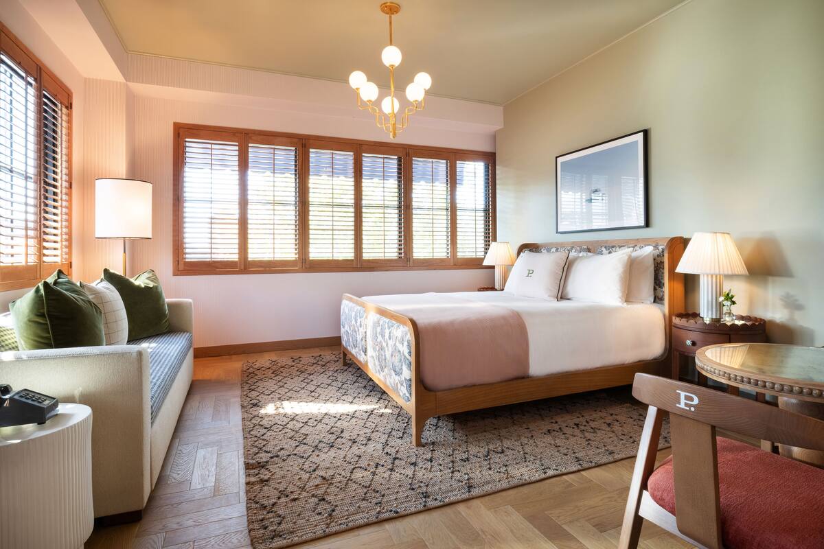 A bedroom with a bed, a sofa, a chair, a desk, and a window with blinds.