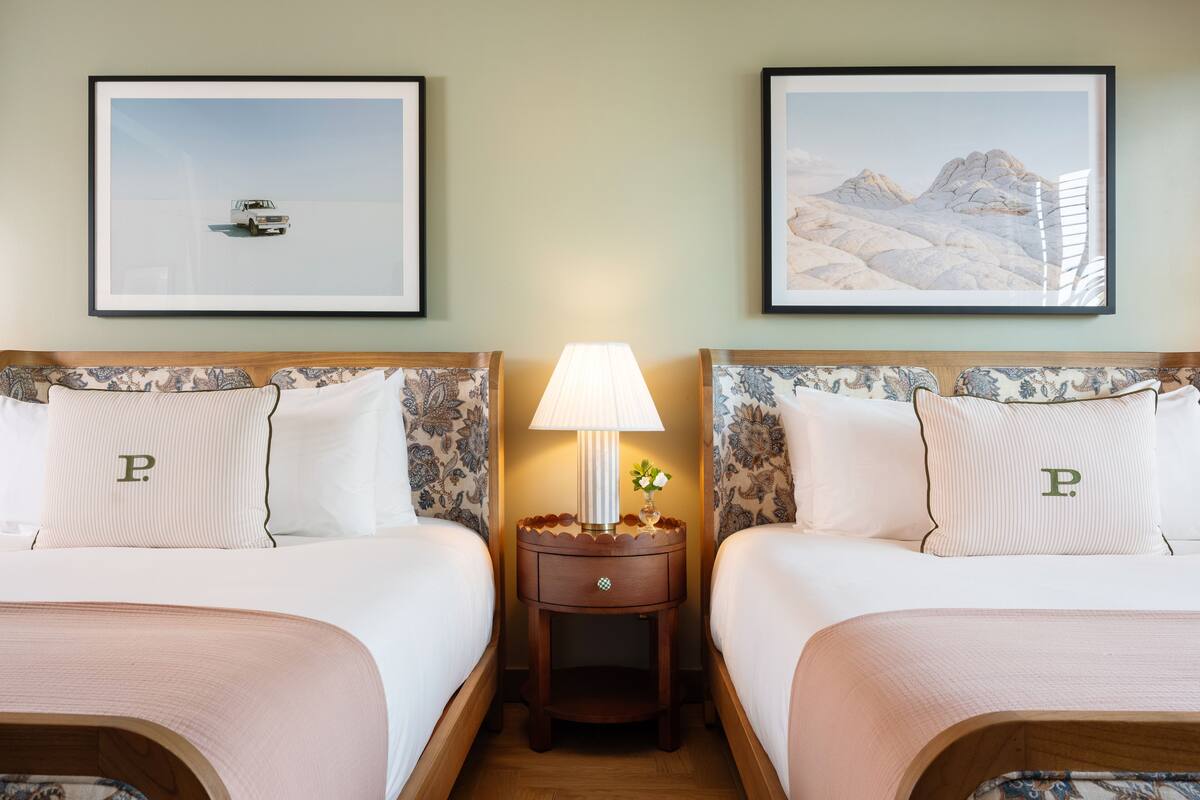 A hotel room with two beds, each with a headboard, a nightstand with a lamp, and framed pictures on the wall.