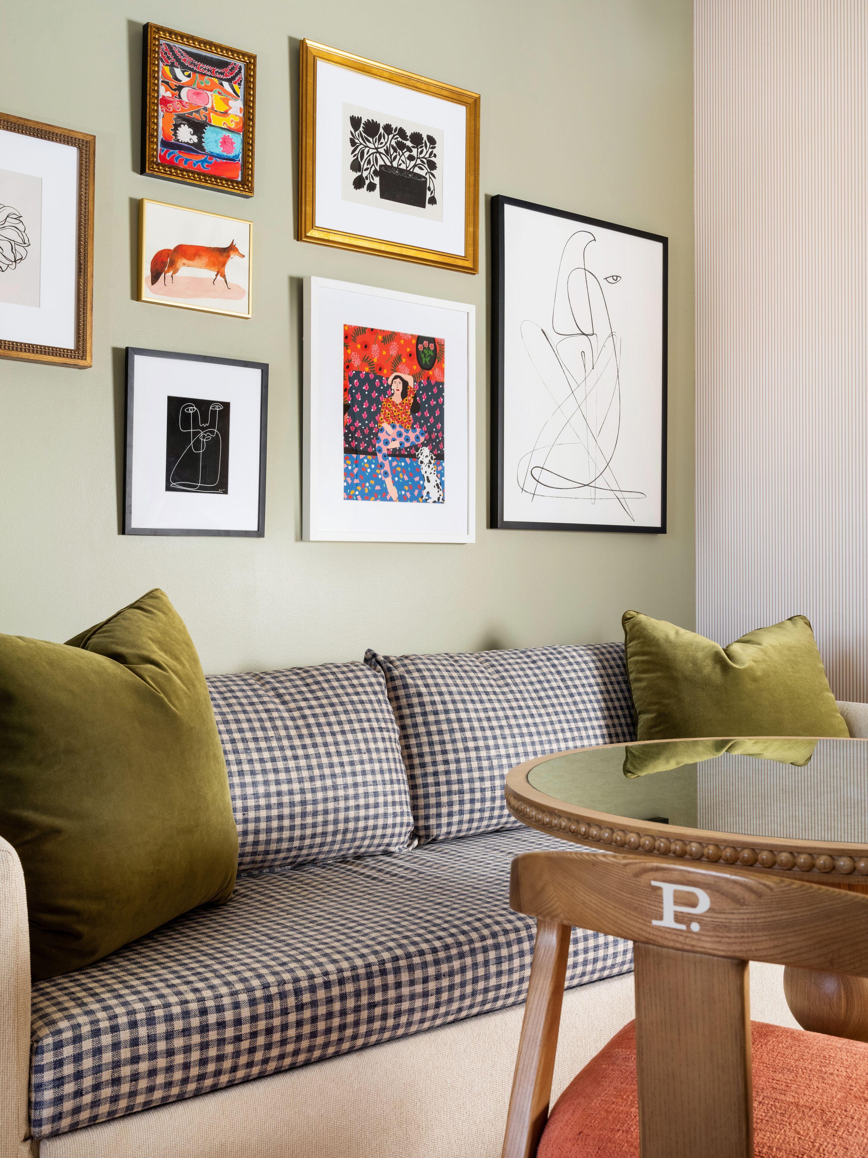 A living room with a checkered sofa, a glass coffee table, and various framed artworks on the wall.